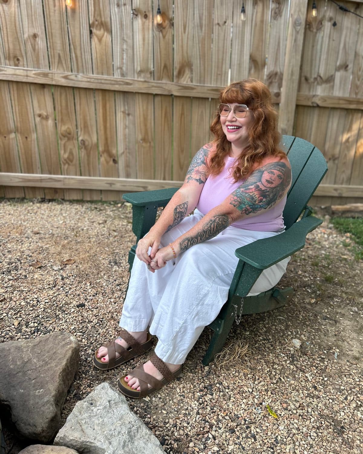 Kierstin smiling in a green Adirondack chair under string lights